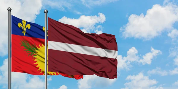 一緒に白い曇り青い空に対して風に振るグアドループとラトビアの旗。外交概念、国際関係. — ストック写真