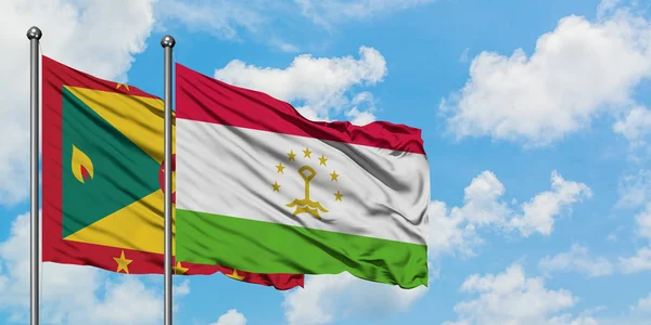 Bandera de Granada y Tayikistán ondeando en el viento contra el cielo azul nublado blanco juntos. Concepto diplomático, relaciones internacionales . — Foto de Stock