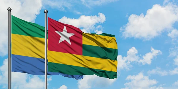 Gabón y Togo bandera ondeando en el viento contra el blanco cielo azul nublado juntos. Concepto diplomático, relaciones internacionales . — Foto de Stock