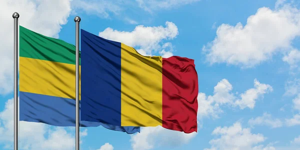 Gabón y Rumania bandera ondeando en el viento contra el cielo azul nublado blanco juntos. Concepto diplomático, relaciones internacionales . — Foto de Stock