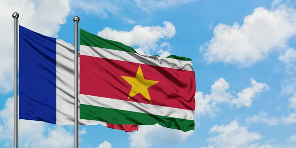 Bandera de Francia y Surinam ondeando en el viento contra el cielo azul nublado blanco juntos. Concepto diplomático, relaciones internacionales . — Foto de Stock