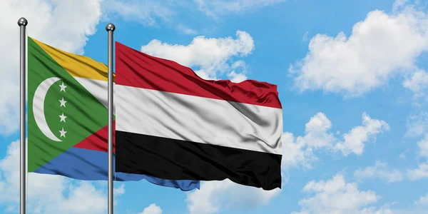 Bandera de las Comoras y Yemen ondeando en el viento contra el cielo azul nublado blanco juntos. Concepto diplomático, relaciones internacionales . — Foto de Stock