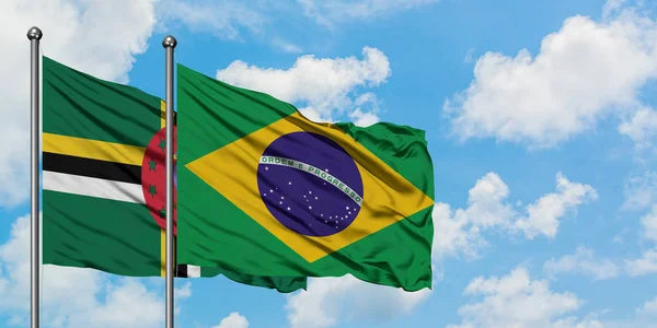 Dominica y la bandera de Brasil ondeando en el viento contra el cielo azul nublado blanco juntos. Concepto diplomático, relaciones internacionales . — Foto de Stock