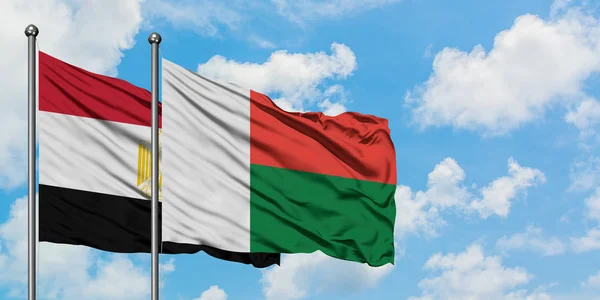 Bandera de Egipto y Madagascar ondeando en el viento contra el cielo azul nublado blanco juntos. Concepto diplomático, relaciones internacionales . — Foto de Stock