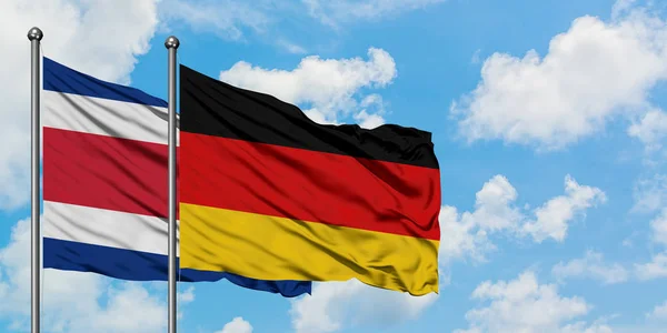 Costa Rica és Németország zászló integetett a szél ellen, fehér felhős kék ég együtt. Diplomáciai koncepció, nemzetközi kapcsolatok. — Stock Fotó