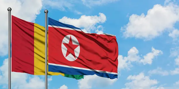 Gine ve Kuzey Kore bayrağı birlikte beyaz bulutlu mavi gökyüzüne karşı rüzgarsal sallayarak. Diplomasi kavramı, uluslararası ilişkiler. — Stok fotoğraf