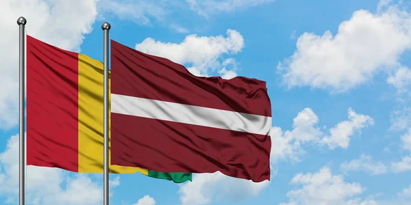 Gwinea i Łotwa flaga machając w wiatr przed białym zachmurzone błękitne niebo razem. Koncepcja dyplomacji, stosunki międzynarodowe. — Zdjęcie stockowe