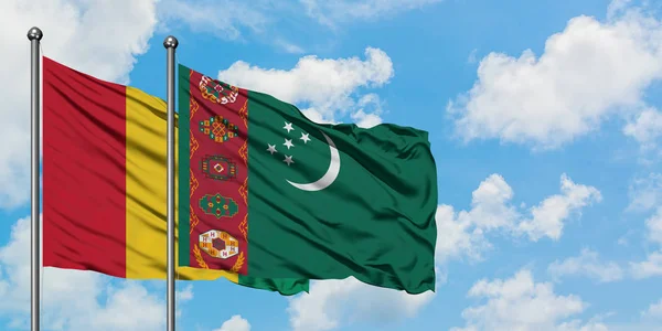 Bandera de Guinea y Turkmenistán ondeando en el viento contra el cielo azul nublado blanco juntos. Concepto diplomático, relaciones internacionales . — Foto de Stock