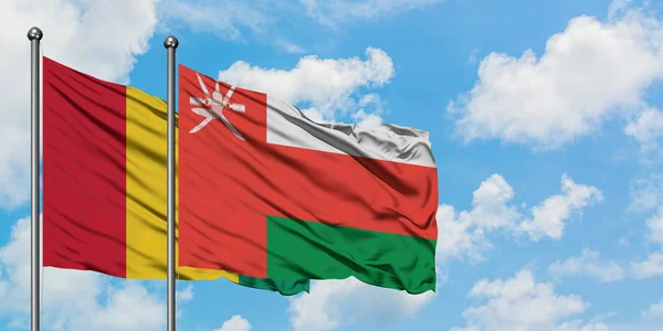 Bandera de Guinea y Omán ondeando en el viento contra el cielo azul nublado blanco juntos. Concepto diplomático, relaciones internacionales . — Foto de Stock