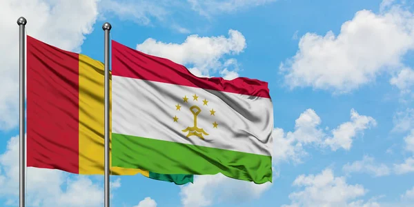 Bandera de Guinea y Tayikistán ondeando en el viento contra el cielo azul nublado blanco juntos. Concepto diplomático, relaciones internacionales . — Foto de Stock