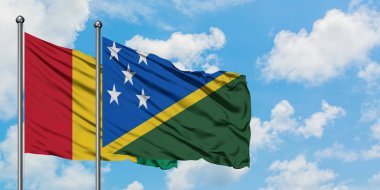 Gine ve Solomon Adaları bayrağı birlikte beyaz bulutlu mavi gökyüzüne karşı rüzgarda sallayarak. Diplomasi kavramı, uluslararası ilişkiler.