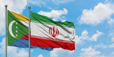 Komorlar ve İran bayrağı birlikte beyaz bulutlu mavi gökyüzüne karşı rüzgarda sallayarak. Diplomasi kavramı, uluslararası ilişkiler.