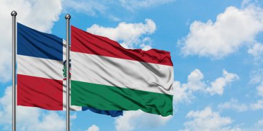 Dominik Cumhuriyeti ve Macaristan bayrağı birlikte beyaz bulutlu mavi gökyüzüne karşı rüzgarda sallayarak. Diplomasi kavramı, uluslararası ilişkiler.