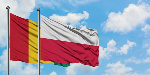 La bandiera della Guinea e della Polonia sventola nel vento contro il bianco cielo blu nuvoloso insieme. Concetto di diplomazia, relazioni internazionali . — Foto Stock