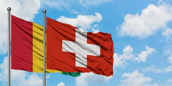 Флаг Гвинеи и Швейцарии размахивает ветром против белого облачно-голубого неба вместе. Концепция дипломатии, международные отношения . — стоковое фото