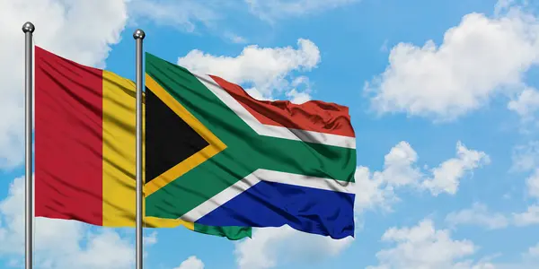 Vlajka Guineje a Jihoafrické republiky mávaje ve větru proti bíle zatažené modré obloze. Diplomacie, mezinárodní vztahy. — Stock fotografie