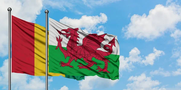 A bandeira da Guiné e do País de Gales agitando no vento contra o céu azul nublado branco juntos. Conceito de diplomacia, relações internacionais . — Fotografia de Stock