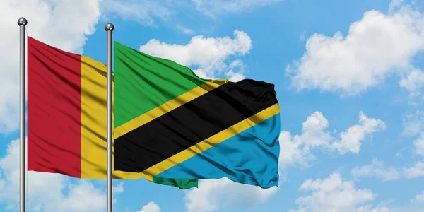 Bandera de Guinea y Tanzania ondeando en el viento contra el cielo azul nublado blanco juntos. Concepto diplomático, relaciones internacionales . — Foto de Stock