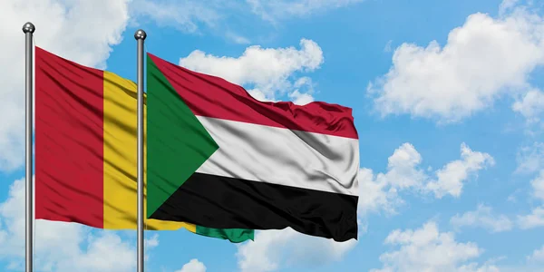 Gine ve Sudan bayrağı birlikte beyaz bulutlu mavi gökyüzüne karşı rüzgarsal sallayarak. Diplomasi kavramı, uluslararası ilişkiler. — Stok fotoğraf