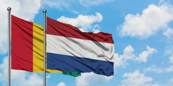 La bandiera della Guinea e dei Paesi Bassi sventola nel vento contro il bianco cielo blu nuvoloso insieme. Concetto di diplomazia, relazioni internazionali . — Foto Stock