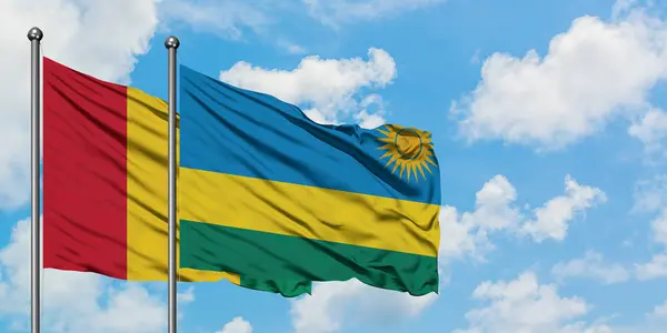 Bandera de Guinea y Ruanda ondeando en el viento contra el cielo azul nublado blanco juntos. Concepto diplomático, relaciones internacionales . — Foto de Stock