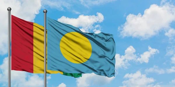 Bandera de Guinea y Palaos ondeando en el viento contra el cielo azul nublado blanco juntos. Concepto diplomático, relaciones internacionales . — Foto de Stock