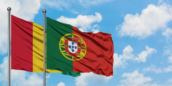 Drapeau de Guinée et Portugal agitant dans le vent contre ciel bleu nuageux blanc ensemble. Concept de diplomatie, relations internationales . — Photo