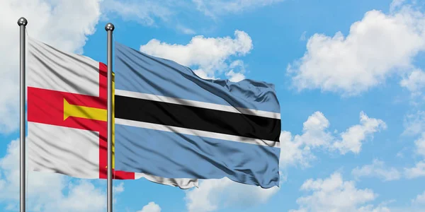 Guernsey e la bandiera del Botswana sventolano insieme nel vento contro il bianco cielo blu nuvoloso. Concetto di diplomazia, relazioni internazionali . — Foto Stock