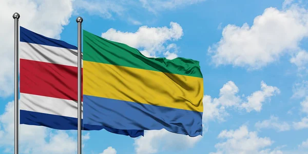 Costa Rica en Gabon vlag zwaaien in de wind tegen witte bewolkte blauwe hemel samen. Diplomatie concept, internationale betrekkingen. — Stockfoto