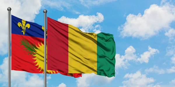 Guadalupe y la bandera de Guinea ondeando en el viento contra el cielo azul nublado blanco juntos. Concepto diplomático, relaciones internacionales . — Foto de Stock