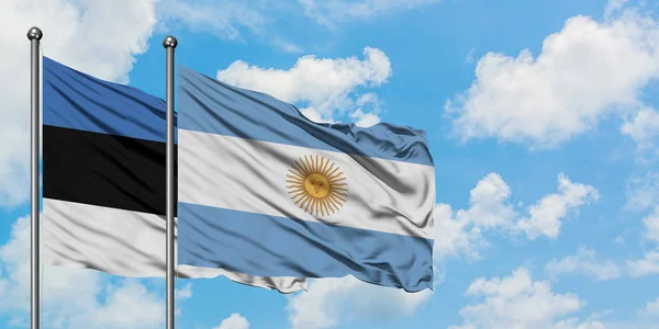 一緒に白い曇り青い空に対して風に手を振るエストニアとアルゼンチンの旗。外交概念、国際関係. — ストック写真