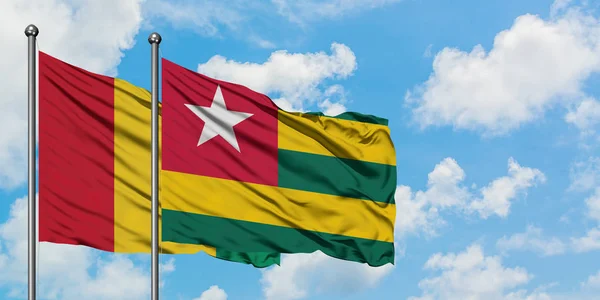Bandera de Guinea y Togo ondeando en el viento contra el cielo azul nublado blanco juntos. Concepto diplomático, relaciones internacionales . — Foto de Stock