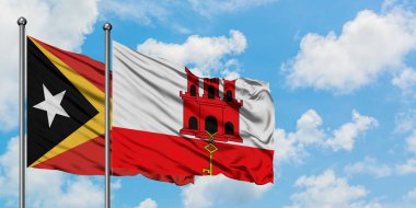 Doğu Timor ve Cebelitarık bayrağı birlikte beyaz bulutlu mavi gökyüzüne karşı rüzgarda sallayarak. Diplomasi kavramı, uluslararası ilişkiler.