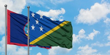 Guam ve Solomon Adaları bayrağı birlikte beyaz bulutlu mavi gökyüzüne karşı rüzgarda sallayarak. Diplomasi kavramı, uluslararası ilişkiler.