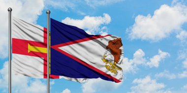 Guernsey ve Amerikan Samoası bayrağı birlikte beyaz bulutlu mavi gökyüzüne karşı rüzgarda sallayarak. Diplomasi kavramı, uluslararası ilişkiler.