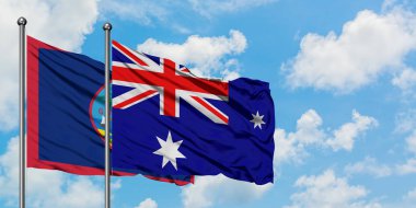 Guam ve Heard Adası ve Mcdonald Adaları bayrağı birlikte beyaz bulutlu mavi gökyüzüne karşı rüzgarda sallayarak. Diplomasi kavramı, uluslararası ilişkiler.