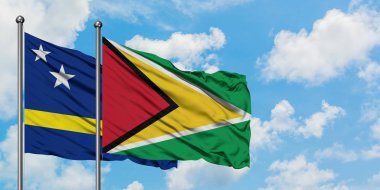 Curacao ve Guyana bayrağı birlikte beyaz bulutlu mavi gökyüzüne karşı rüzgarda sallayarak. Diplomasi kavramı, uluslararası ilişkiler.