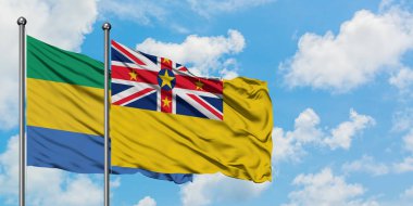 Gabon ve Niue bayrağı birlikte beyaz bulutlu mavi gökyüzüne karşı rüzgarda sallayarak. Diplomasi kavramı, uluslararası ilişkiler.