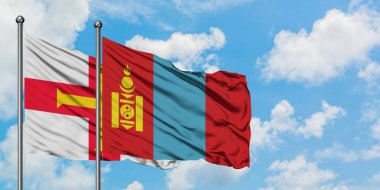 Guernsey ve Moğolistan bayrağı birlikte beyaz bulutlu mavi gökyüzüne karşı rüzgarda sallayarak. Diplomasi kavramı, uluslararası ilişkiler.