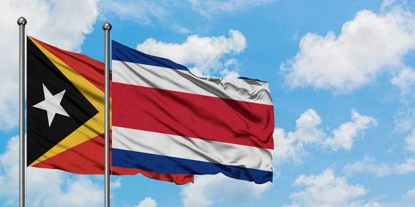 Timor Oriental y la bandera de Costa Rica ondeando en el viento contra el cielo azul nublado blanco juntos. Concepto diplomático, relaciones internacionales . — Foto de Stock