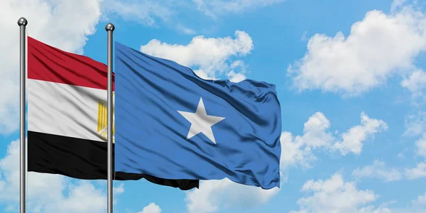 Bandera de Egipto y Somalia ondeando en el viento contra el cielo azul nublado blanco juntos. Concepto diplomático, relaciones internacionales . — Foto de Stock