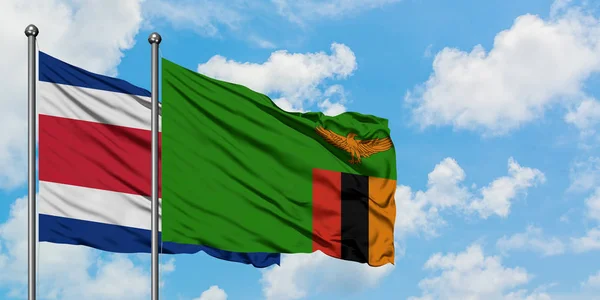 Bandera de Costa Rica y Zambia ondeando en el viento contra el cielo azul nublado blanco juntos. Concepto diplomático, relaciones internacionales . — Foto de Stock