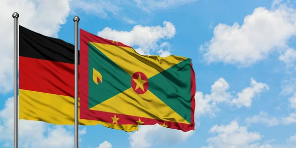 Deutschland und die Grenada-Flagge wehen gemeinsam im Wind gegen den wolkenverhangenen blauen Himmel. Diplomatie-Konzept, internationale Beziehungen. — Stockfoto