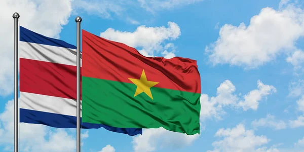 Bandera de Costa Rica y Burkina Faso ondeando en el viento contra el cielo azul nublado blanco juntos. Concepto diplomático, relaciones internacionales . — Foto de Stock