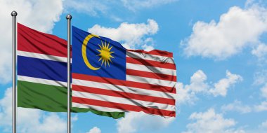 Gambiya ve Malezya bayrağı birlikte beyaz bulutlu mavi gökyüzüne karşı rüzgarda sallayarak. Diplomasi kavramı, uluslararası ilişkiler.