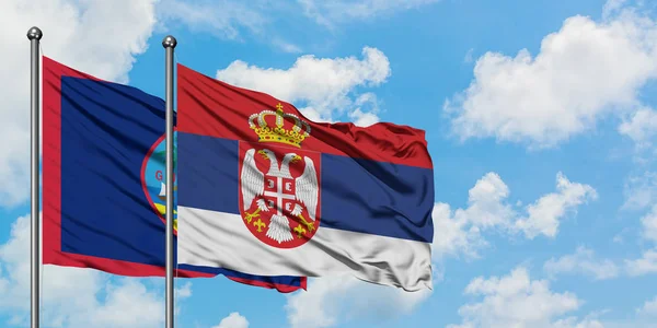 Bandera de Guam y Serbia ondeando en el viento contra el cielo azul nublado blanco juntos. Concepto diplomático, relaciones internacionales . — Foto de Stock