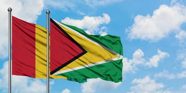 Guinea e Guyana sventolano nel vento contro il bianco cielo blu nuvoloso insieme. Concetto di diplomazia, relazioni internazionali . — Foto Stock