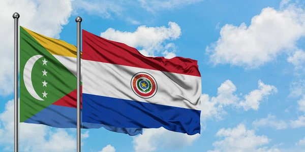 Bandera de las Comoras y Paraguay ondeando en el viento contra el cielo azul nublado blanco juntos. Concepto diplomático, relaciones internacionales . — Foto de Stock