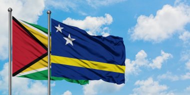 Guyana ve Curacao bayrağı birlikte beyaz bulutlu mavi gökyüzüne karşı rüzgarda sallayarak. Diplomasi kavramı, uluslararası ilişkiler.