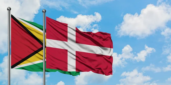 Bandera de Guyana y Dinamarca ondeando en el viento contra el cielo azul nublado blanco juntos. Concepto diplomático, relaciones internacionales . — Foto de Stock